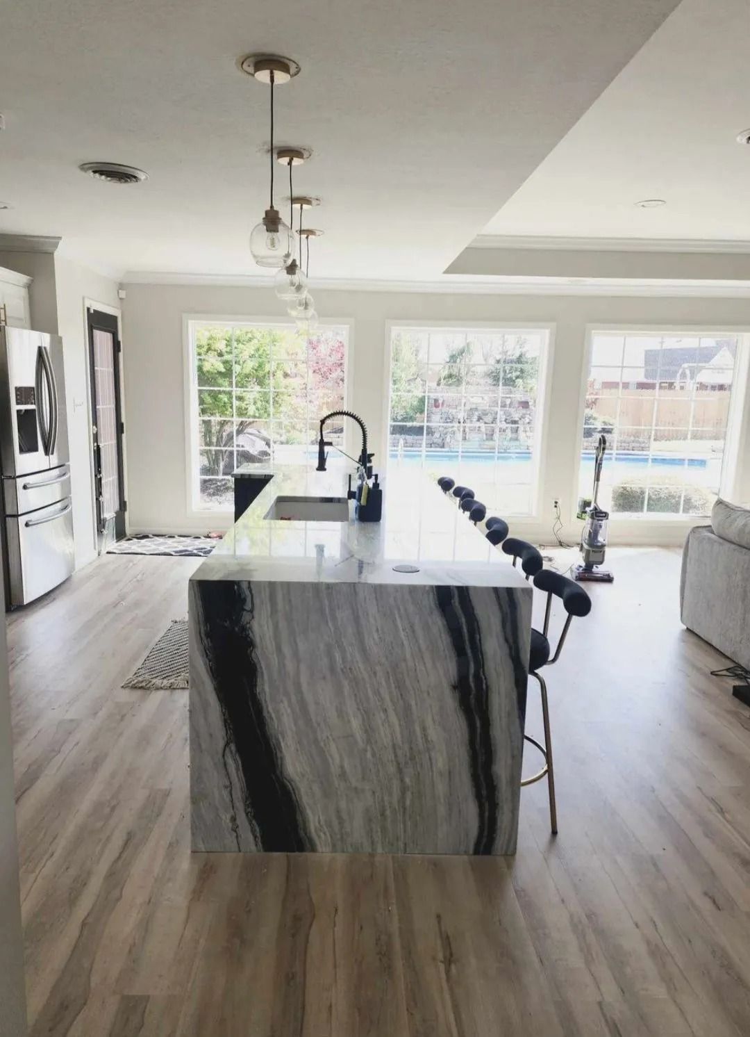 Kitchen with marble island, pendant lights, sink, and large windows overlooking a pool.