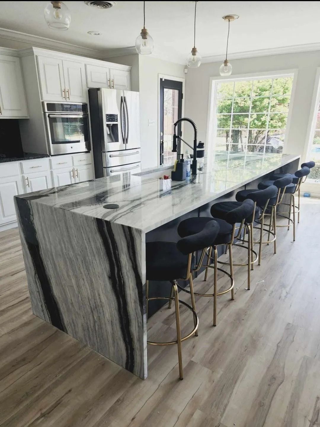 Modern kitchen with a black and white marble island, black bar stools, and white cabinets.