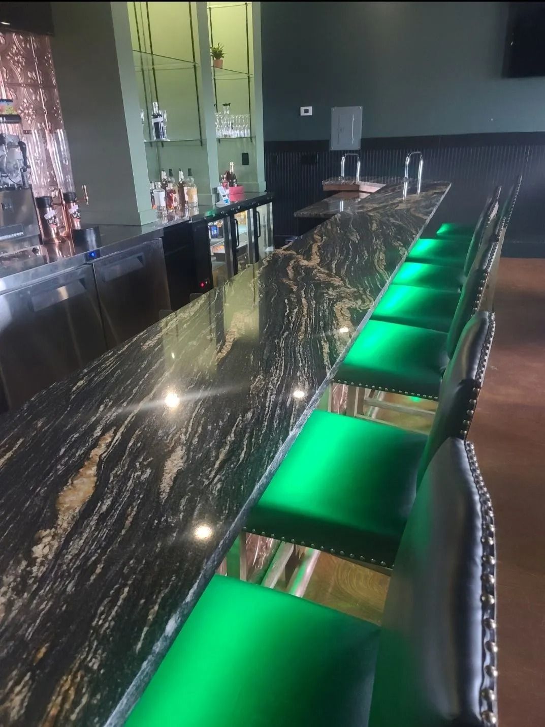 Bar with black granite countertop, green illuminated bar stools, and liquor display in a restaurant.
