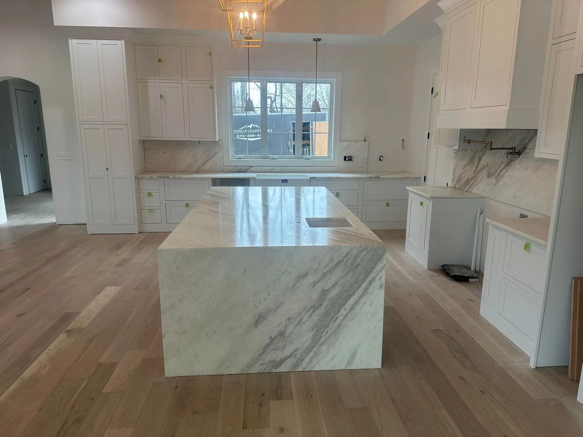 Newly constructed kitchen with white cabinets, marble countertops, and light wood flooring.