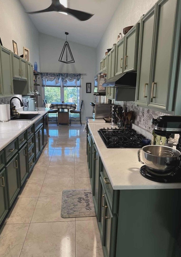 Long kitchen with sage green cabinets, white countertops, and stainless steel appliances.