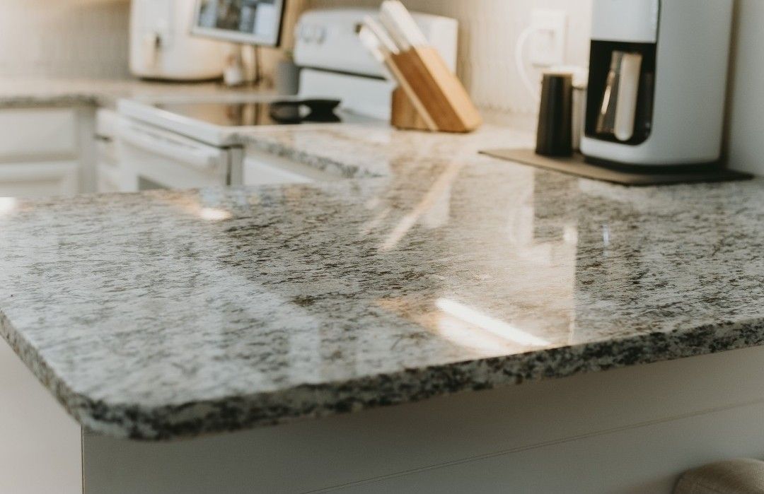 Granite kitchen countertop, light gray with speckled patterns, reflecting light.