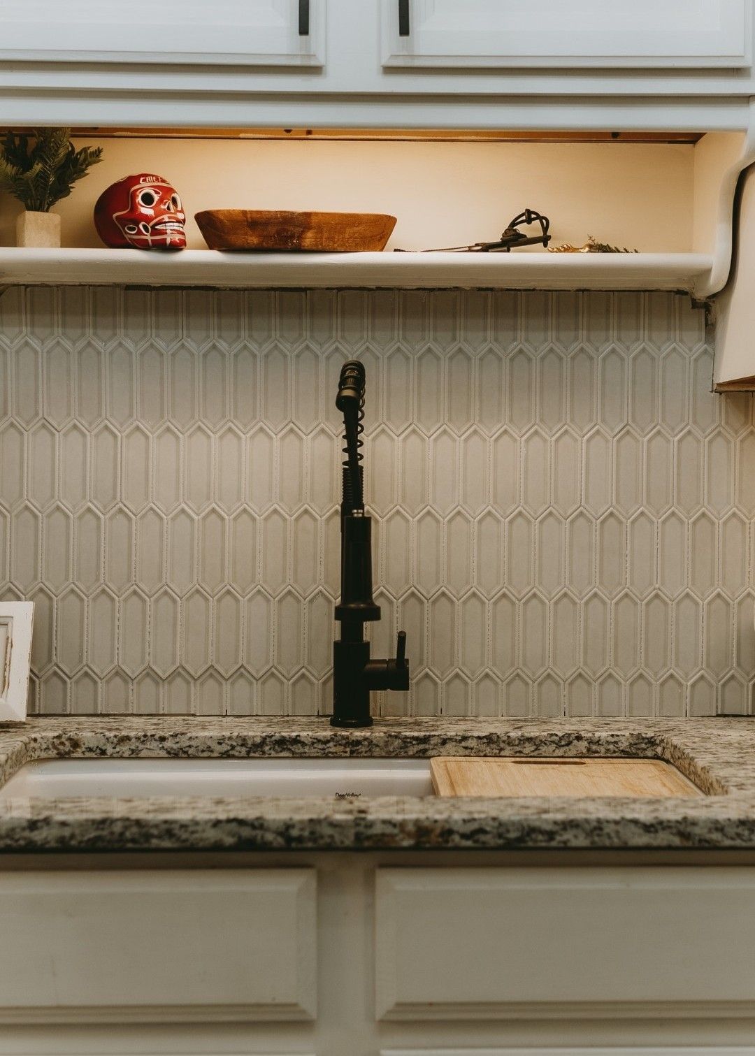 Black faucet over a white sink in a kitchen with white tile backsplash and shelf.