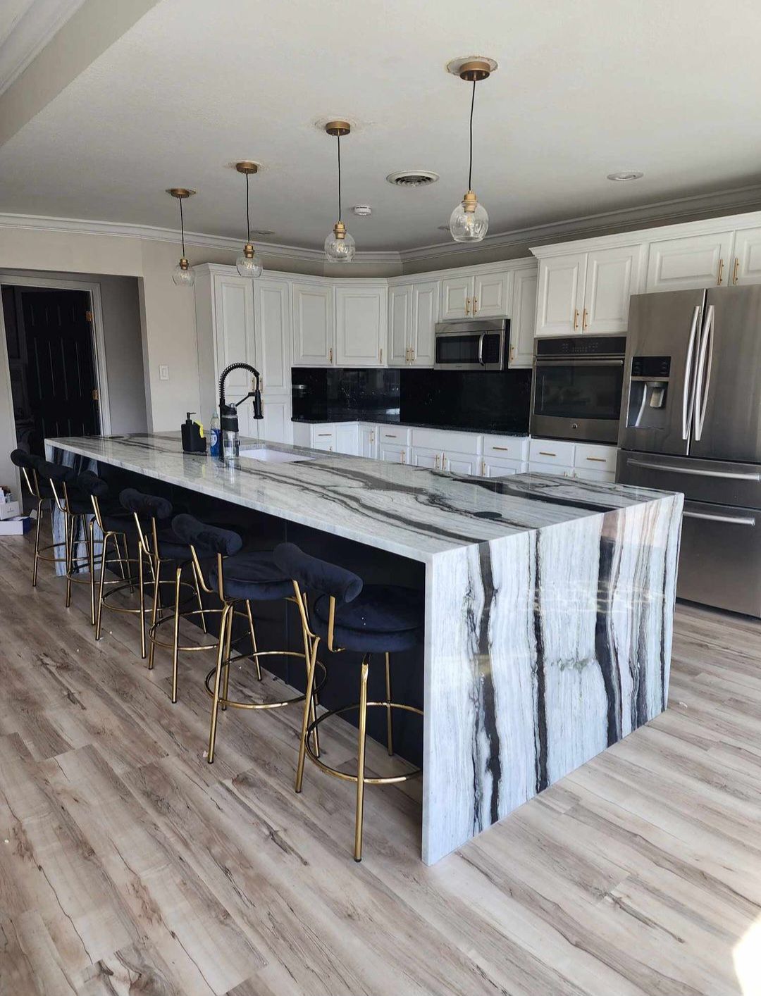 Kitchen with a large island featuring a black and white stone countertop and gold-legged bar stools.