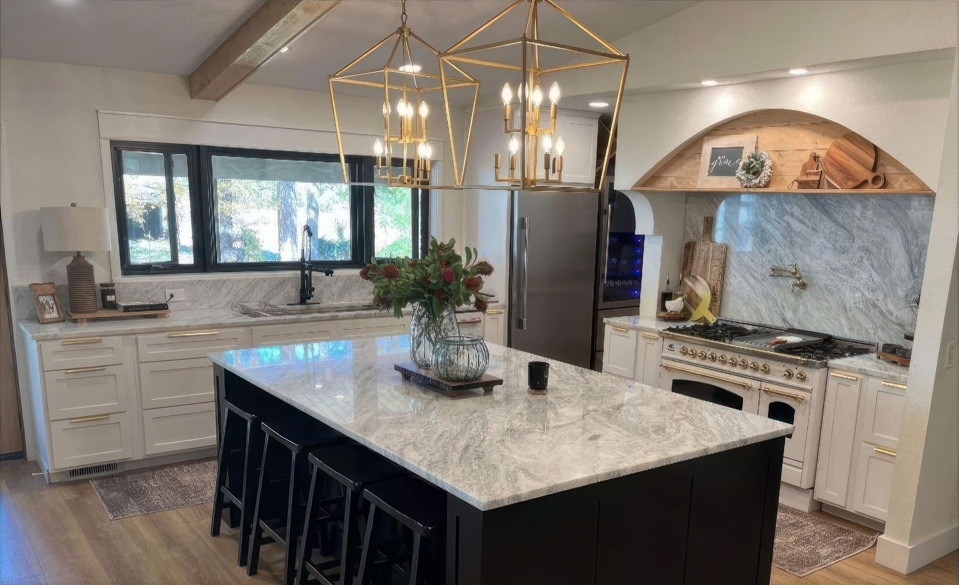 Elegant kitchen with marble countertops, black island, gold light fixtures, and stainless steel refrigerator.