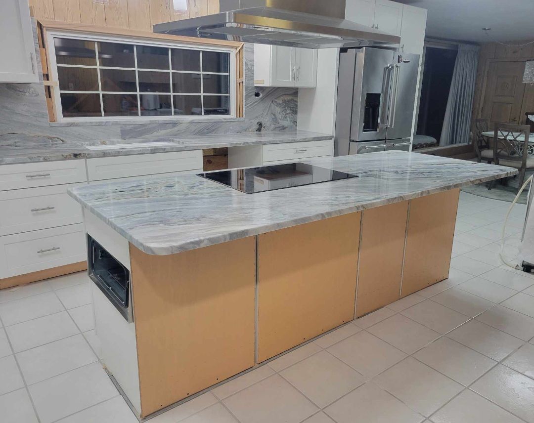 Kitchen island with a marble countertop and built-in stovetop, surrounded by light-colored cabinets.
