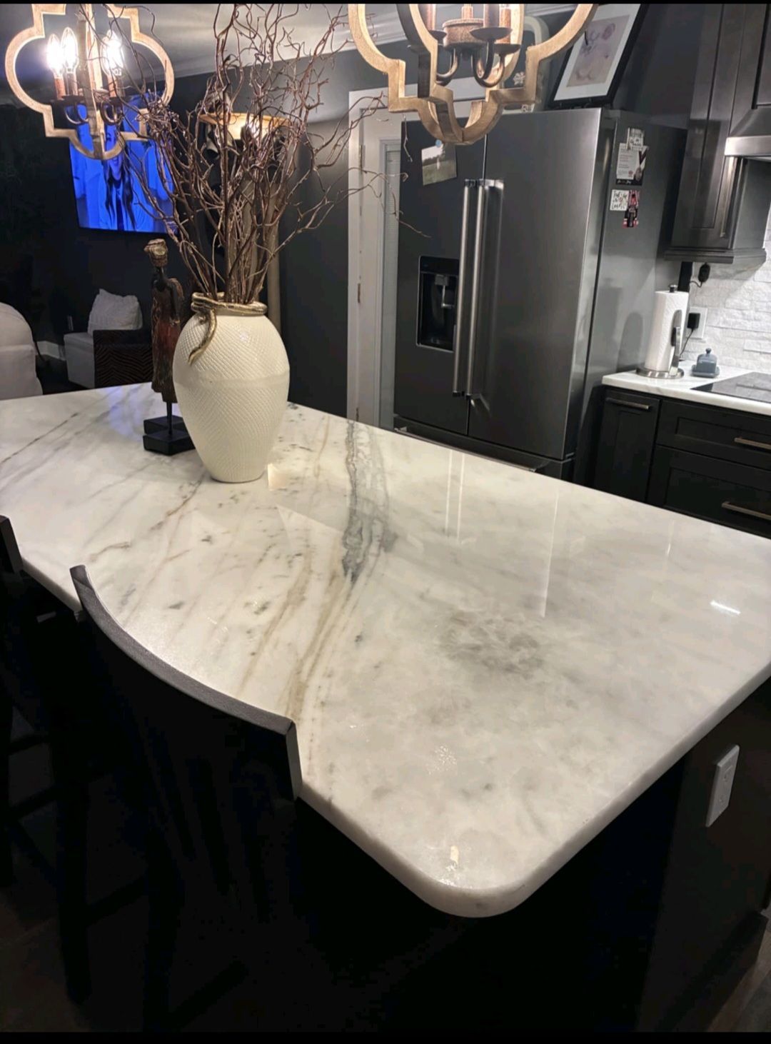Kitchen island with white marble countertop, black cabinets. A vase with dried branches.