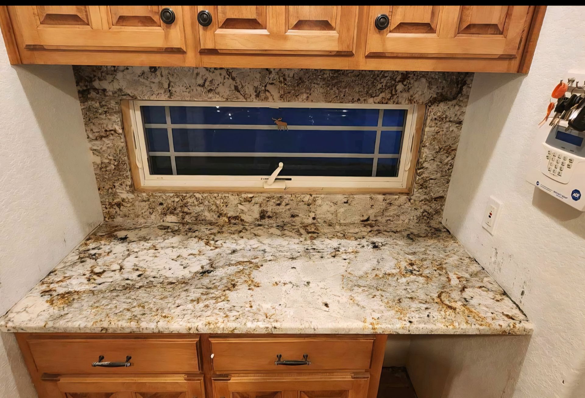 Kitchen countertop with granite backsplash and cabinets above and below, a window is centered.