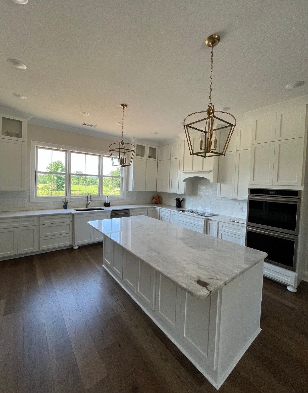 Spacious white kitchen with island, wooden floors, and brass pendant lights.