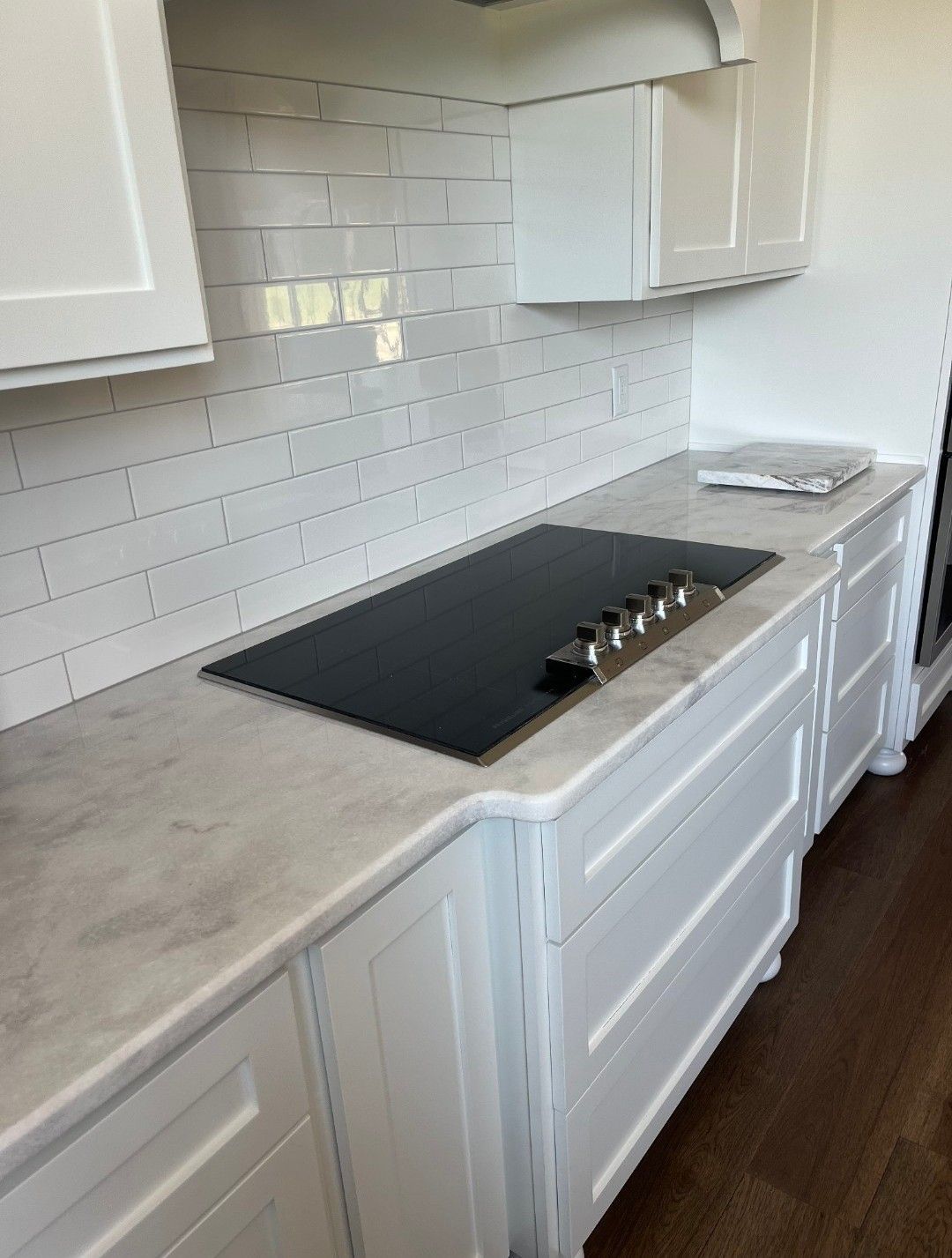 White kitchen with a black stovetop, white cabinets, and marble countertops.