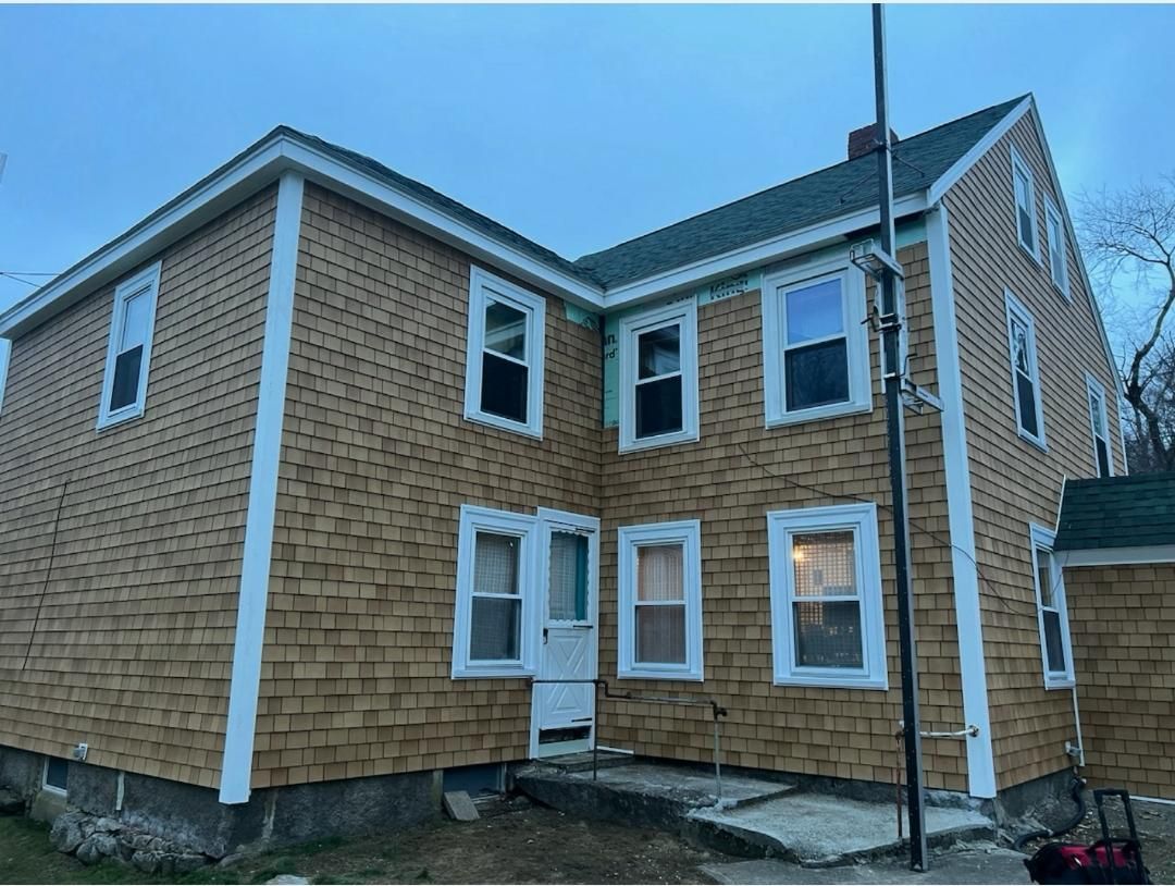 Rear view of a tan vinyl-sided house with white trim and a brick foundation under a blue sky