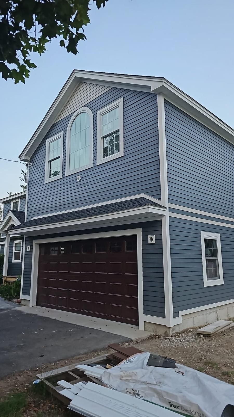 Blue two-story house with white trim and a brown garage door, viewed from the driveway.