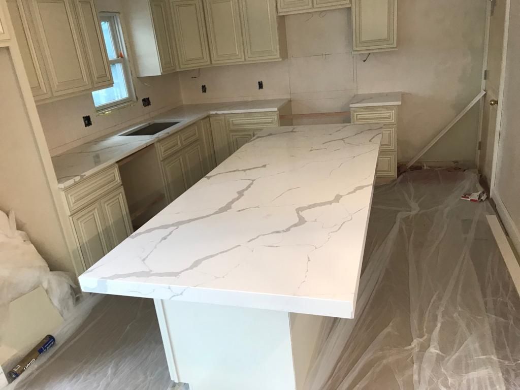 Kitchen with white cabinets and a large white marble island under renovation, floor covered in protective plastic.