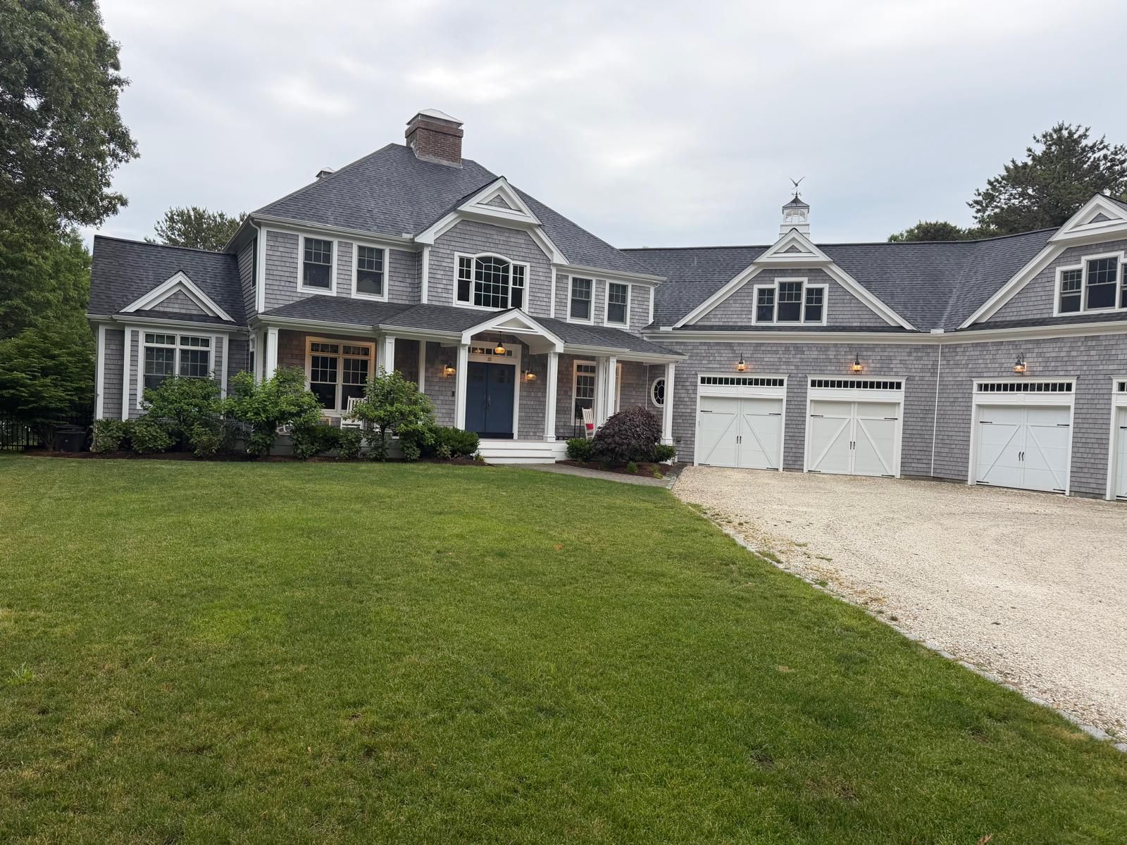 Large gray house with white trim, three-car garage, and gravel driveway beside a green lawn