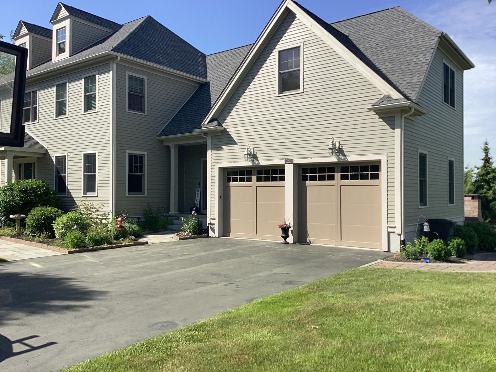 Suburban house with beige siding, two garage doors, driveway, and green lawn on a sunny day
