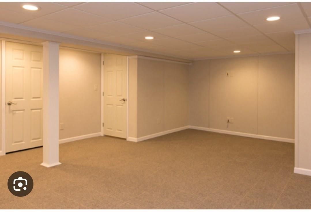Empty beige carpeted room with white columns, closed doors, and recessed ceiling lights