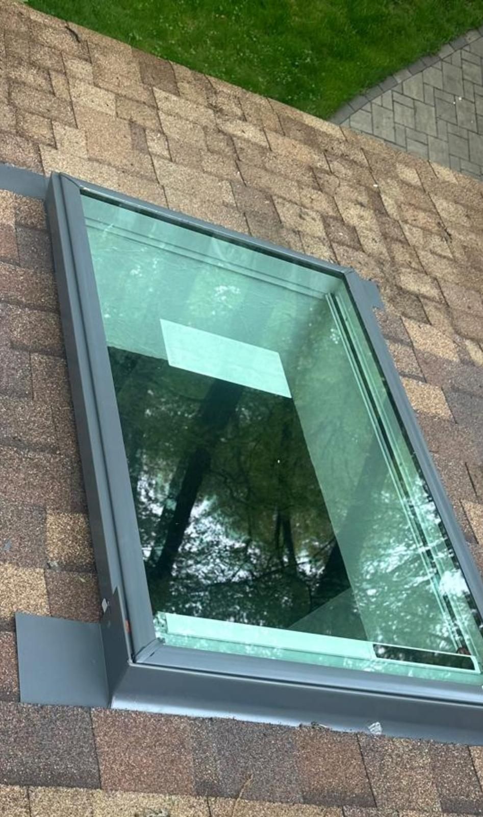 Tilted skylight window in a brick wall, reflecting trees and sky.