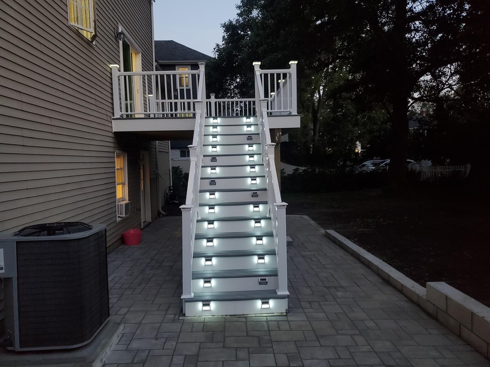Lit outdoor staircase leading to a deck beside a house at dusk