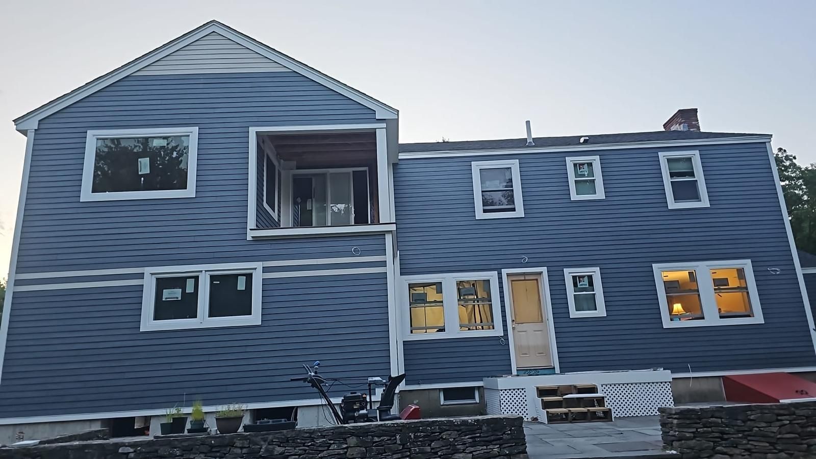 Blue two-story house with lit windows and a large lower-level addition, viewed from outside in winter.