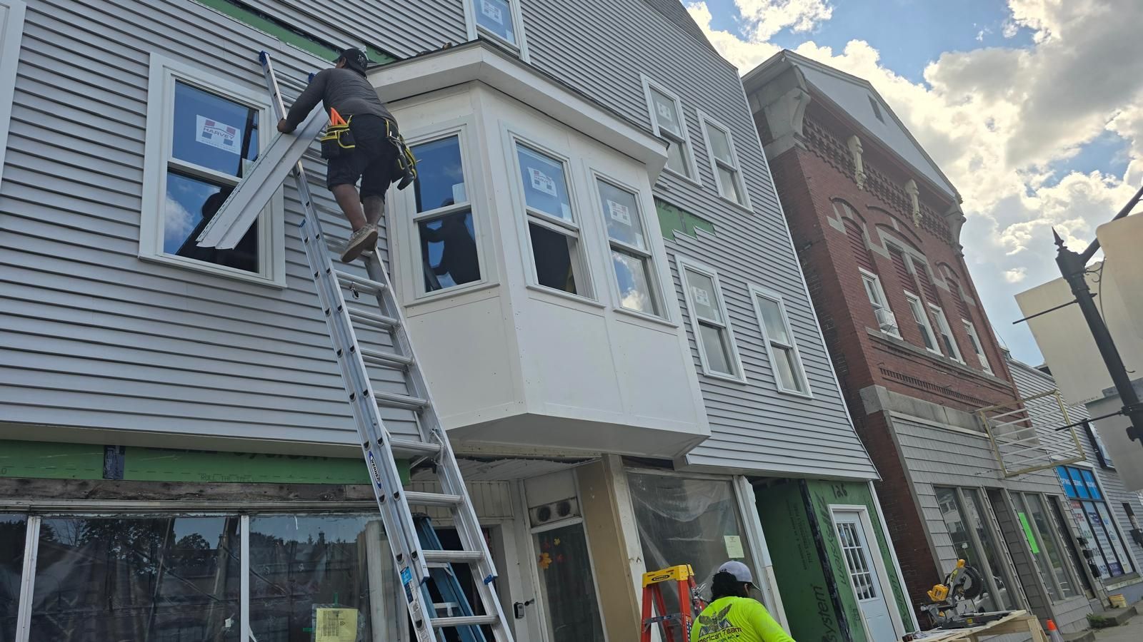 Worker on a ladder repairing the exterior of a gray townhouse on a city street