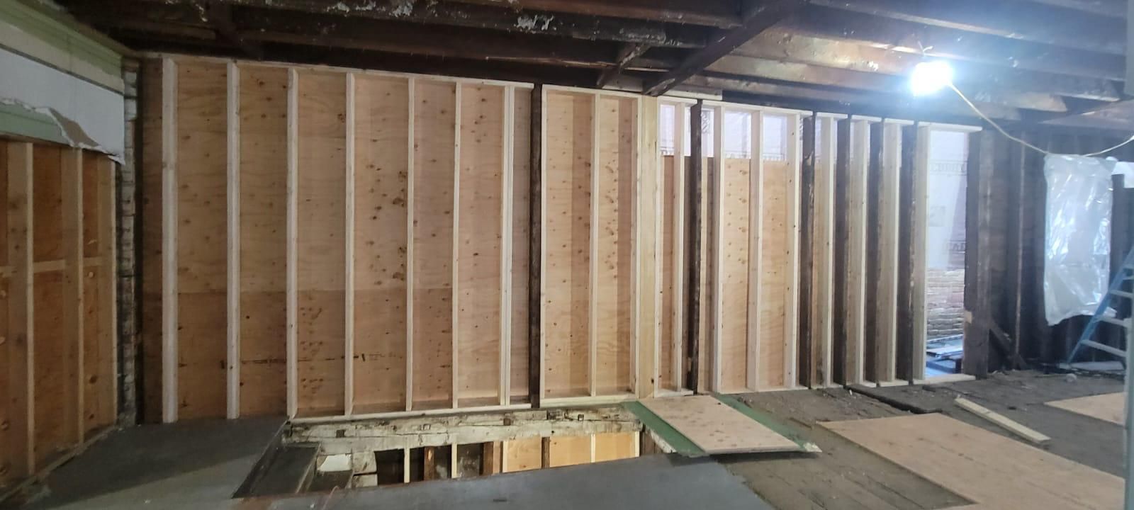 Unfinished basement with framed wooden walls, exposed ceiling joists, and construction materials on the floor