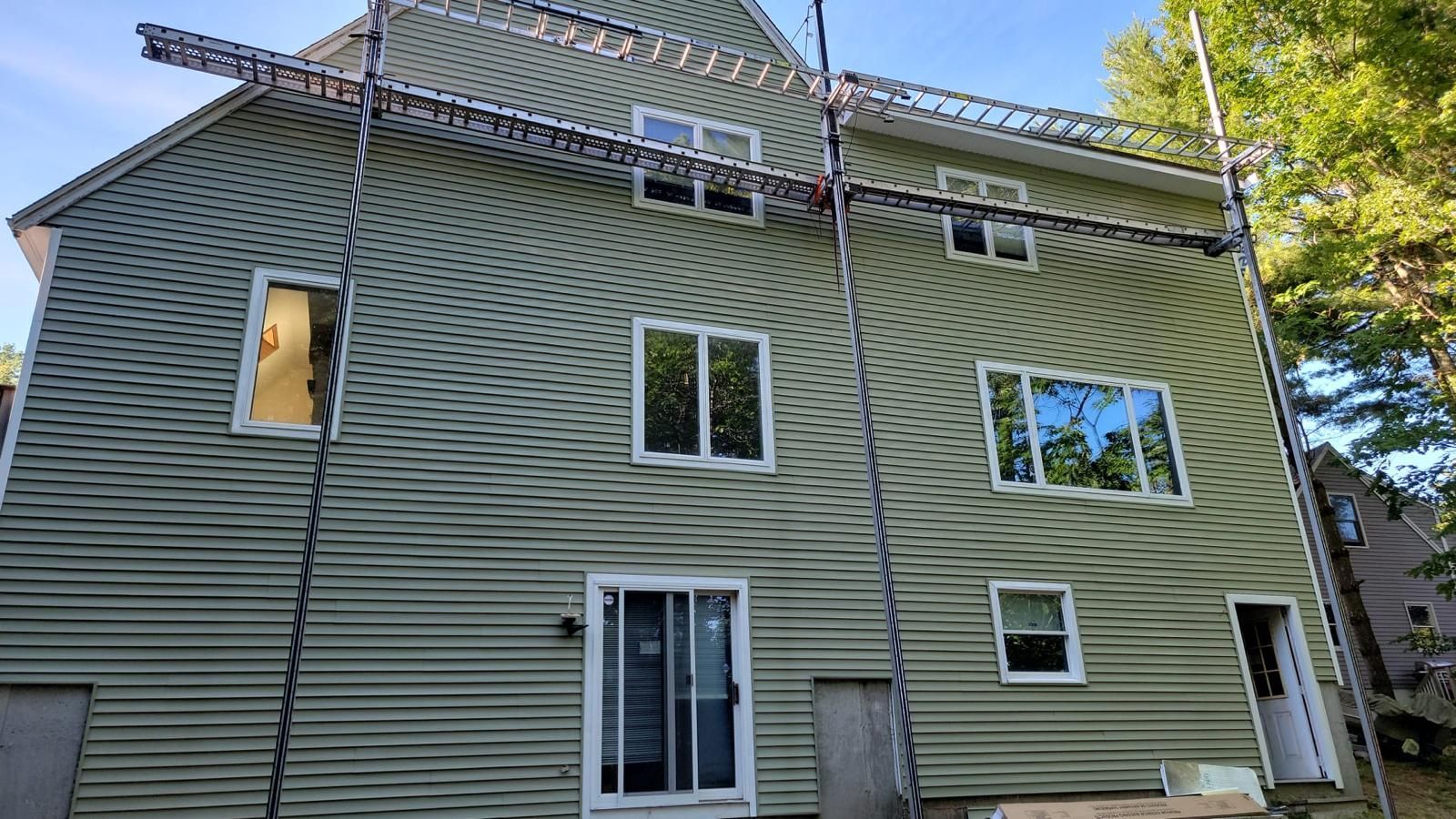 Green-sided house with multiple windows and a ladder leaning against the roofline outdoors