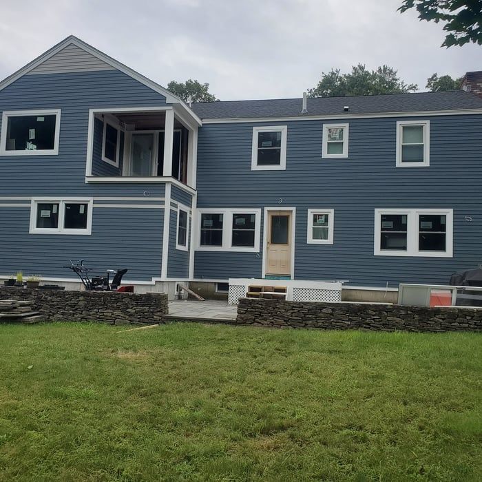 Blue two-story house with white trim and a large lawn, viewed from the backyard.