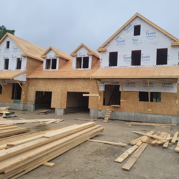 Row of wood-framed houses under construction with lumber stacks in front and cloudy sky above