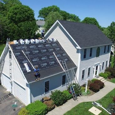 Workers installing a new shingled roof on a white two-story house