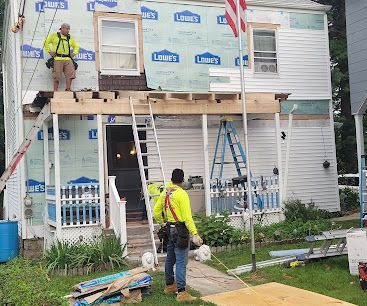 Construction workers on a house scaffold installing siding and windows, with ladders and building materials below.