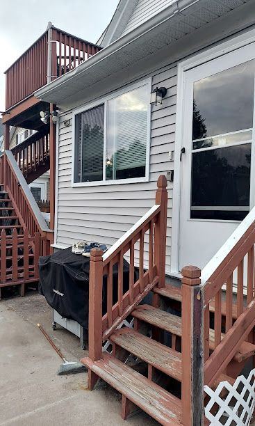 Apartment exterior with white siding, wooden stairs, and a glass door under a gray roof