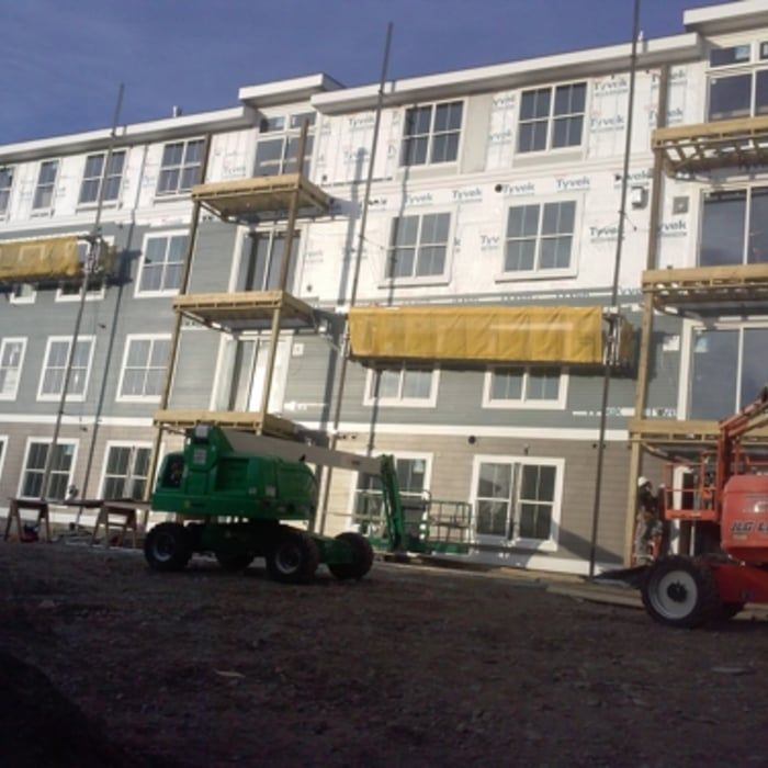 Apartment building under construction with scaffolding and two boom lifts in front