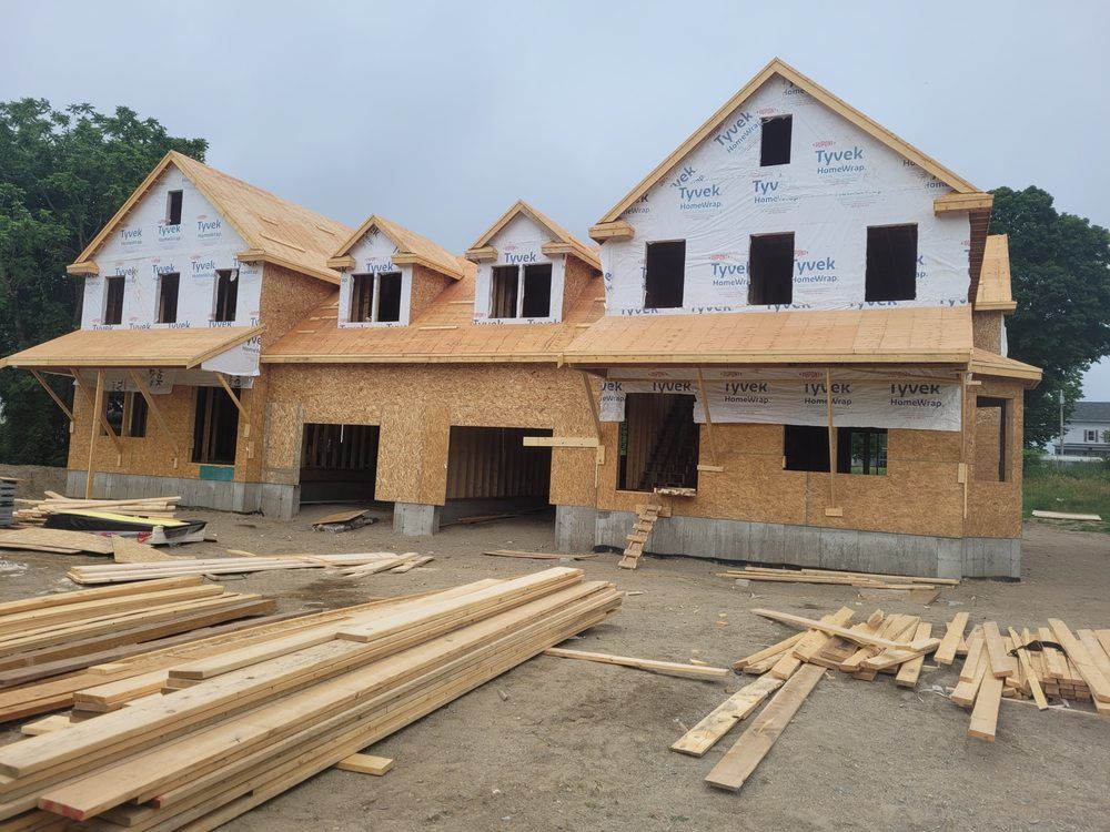 New house under construction with exposed wood framing, roofing, and lumber stacks in front