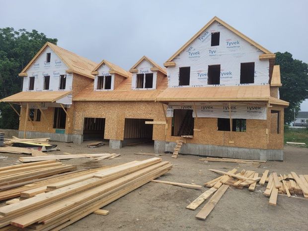 Partially built two-story house with exposed wood framing and lumber piles in front