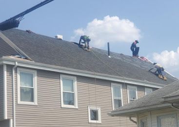 Roofers working on a gray house roof under a blue sky with clouds