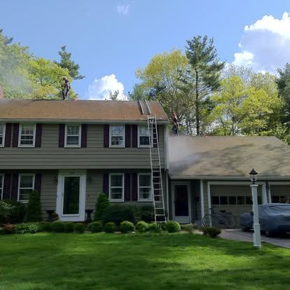Two-story green house with attached garage, white-trimmed windows, and ladder on the roof under a blue sky.