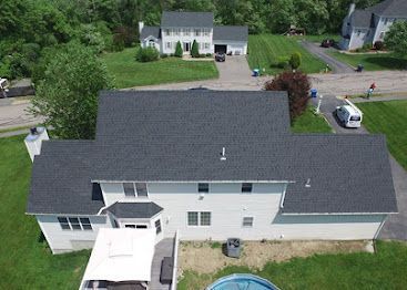 Aerial view of a suburban house with a gray roof, backyard, and driveway with parked vehicles