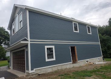 Blue two-story house with white trim, garage, and unfinished lower-level doorway on a sloped lot