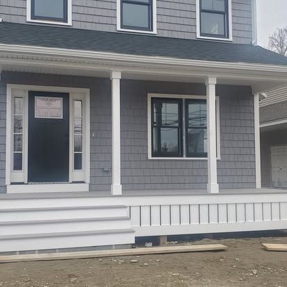 Gray house front with white porch columns, steps, and trim under construction.