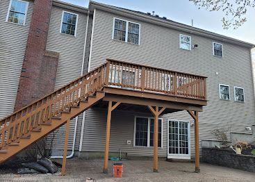 Wooden deck and stairs attached to a beige house, with a covered patio below.