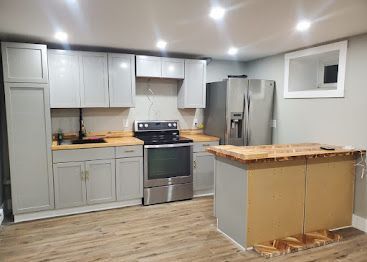 Modern kitchen with gray cabinets, stainless steel appliances, light wood floors, and a wooden island under recessed lights