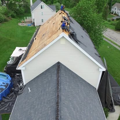 Roofers replacing shingles on a house roof, with exposed plywood and dark new shingles installed on one side.