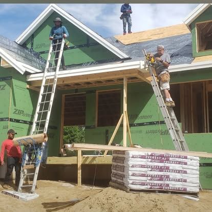 Construction workers installing roof panels on a house under construction, with ladders and lumber in front.