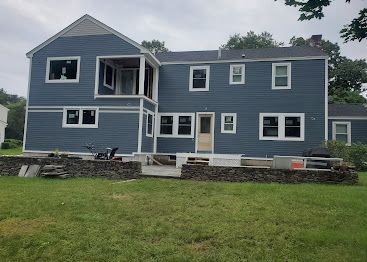 Blue two-story house with white trim and a large grassy yard, viewed from the back.