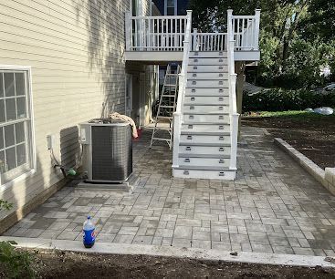 Backyard patio with white stairs to a raised deck, air conditioner unit, and a water bottle on the pavers.