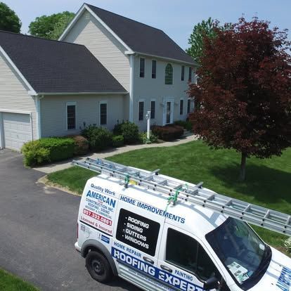 Roofing company van parked in a suburban driveway beside a light gray house and lawn