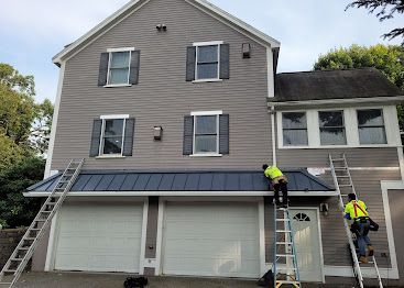 Workers repairing roof on a gray house with ladders and a garage below.