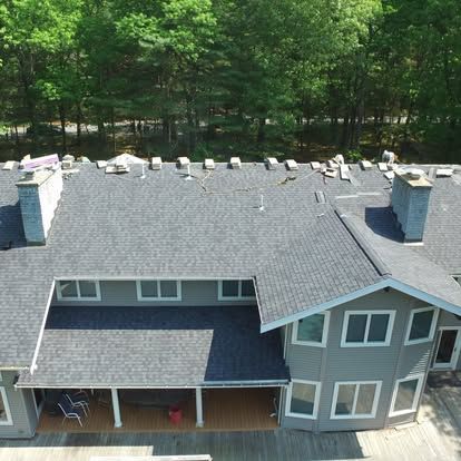 Aerial view of a gray two-story house with a dark roof and wooded backyard.