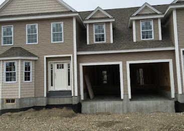 Row of beige townhouses with white trim and two unfinished garage openings on a gravel lot