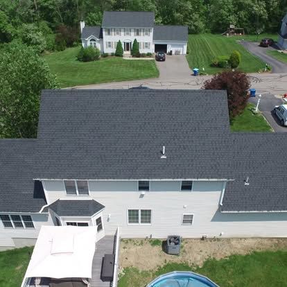 Aerial view of a white suburban house with gray roof, driveway, and green yard.